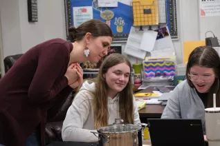 teacher standing over student's desk helping them