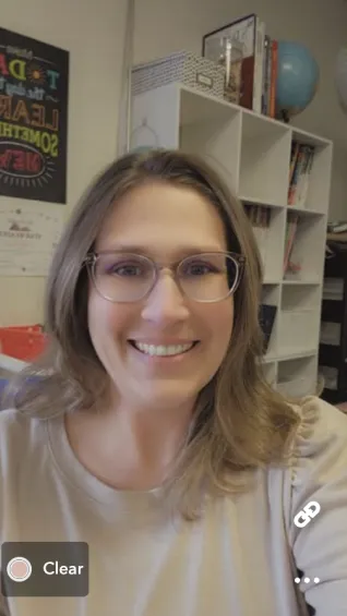 Woman with glasses, smiling, in classroom setting.