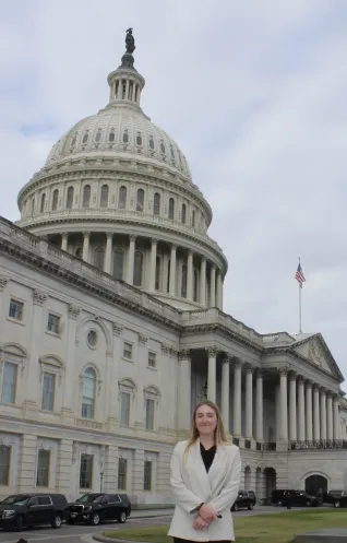 Young woman in white blazer, standing in front of U.S. Capitol building