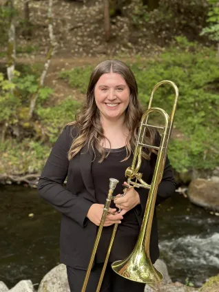 Young woman outdoors, holding a trombone.
