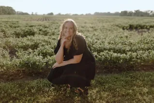 Young woman dressed in black, crouched down in a field.