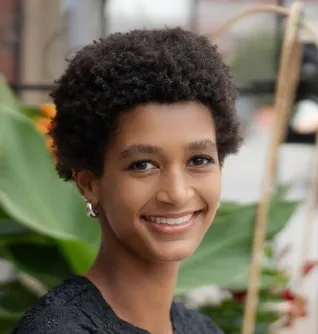 Young woman with short hair smiling in front of plant.