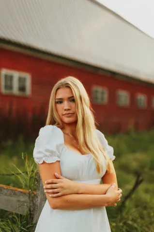 Young woman in white dress, standing in front of red building.