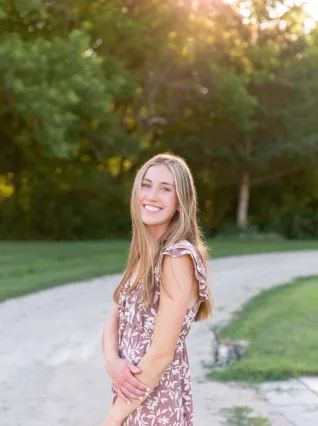Young woman smiling while standing on sidewalk in a park.