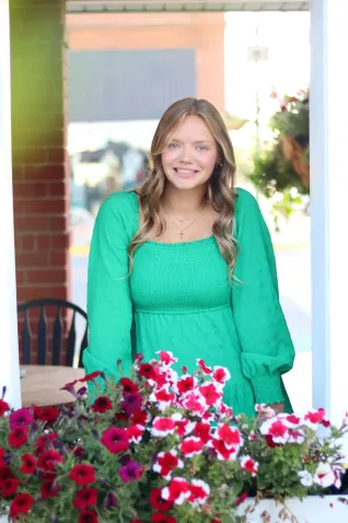 Young woman in green dress smiles for photo with pink flowers in foreground.