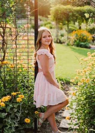 Young woman in pink dress standing in garden with sunflowers in foreground.