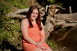 Young woman in orange dress, sitting outside near fallen tree