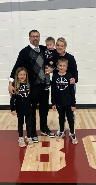A family of five - two adults and three young children - all wearing black outfits, standing in a gymnasium