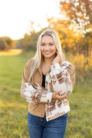 Young woman wearing white and tan jacket, standing in field.