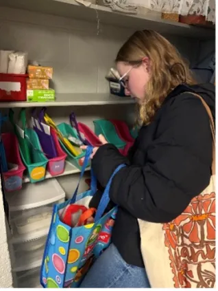 A student sorts items into a colorful reusable bag on shelving stocked with multiple small storage bins.