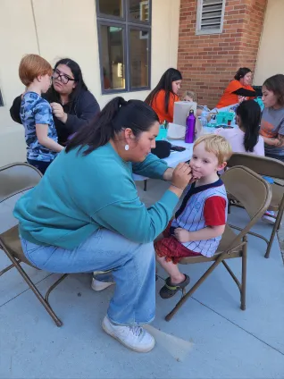 Student members of the United Tribes Technical College Student Education Association paint children's faces during a community event, providing family-friendly activities as part of the chapter's community outreach.