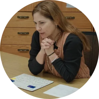 A teacher sits at a round table speaking with students during a small-group reading lesson in an elementary classroom.