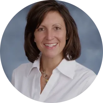 Woman with shoulder-length, brown hair, wearing white, collared shirt, in front of light black backdrop.