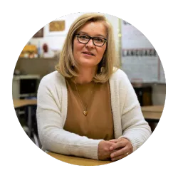 woman with blonde hair wearing glasses and a sweater sitting at a desk