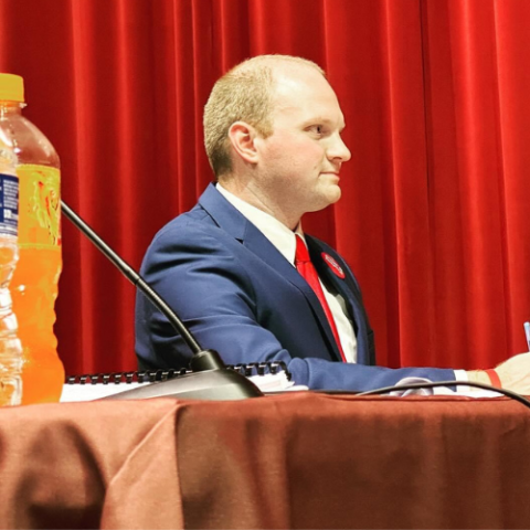 man in suit sitting at a panel on stage