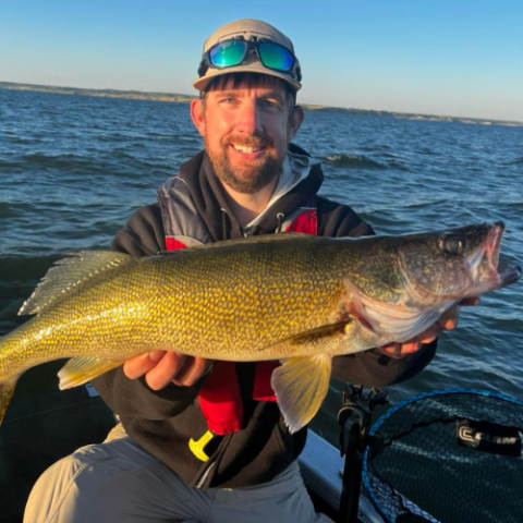 fisherman holding large fish in a boat on a lake